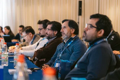 Público sentado observa una charla desde un costado de la sala.