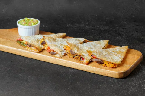 Quesadillas acompañadas de guacamole sobre una tabla de madera.