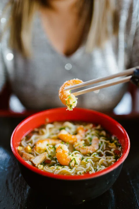 Ramen servido en bowl mientras una persona usa palillos.