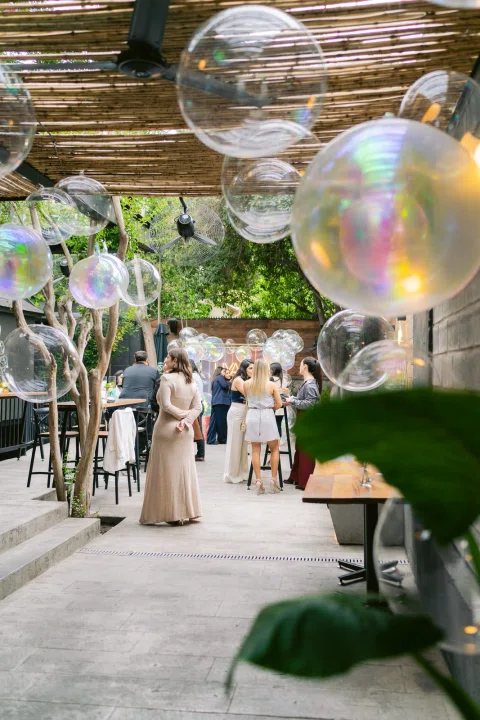 Recepción exterior decorada con globos iridiscentes y mesas para invitados.