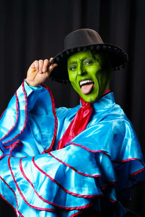 Retrato de artista con maquillaje verde, sombrero y vestuario colorido.