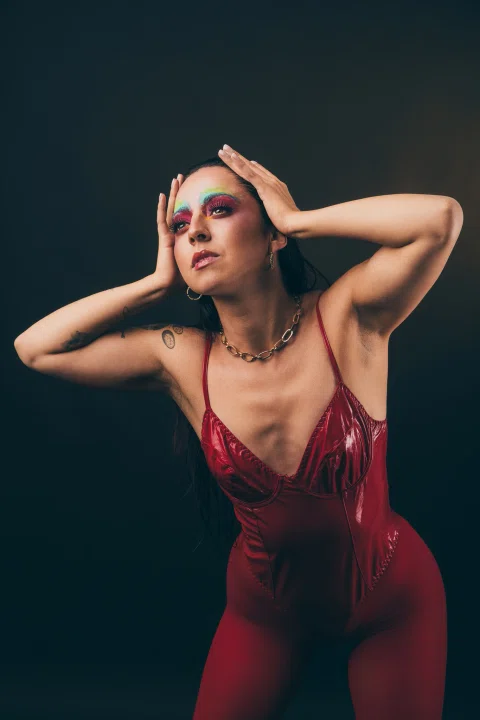 Retrato artístico de una mujer con vestuario rojo y pose expresiva sobre fondo oscuro.