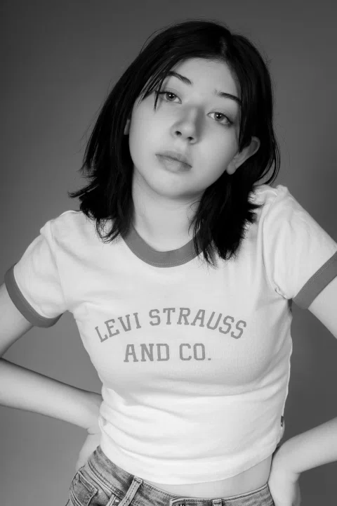 Retrato en blanco y negro de una mujer joven con camiseta clara sobre fondo oscuro.