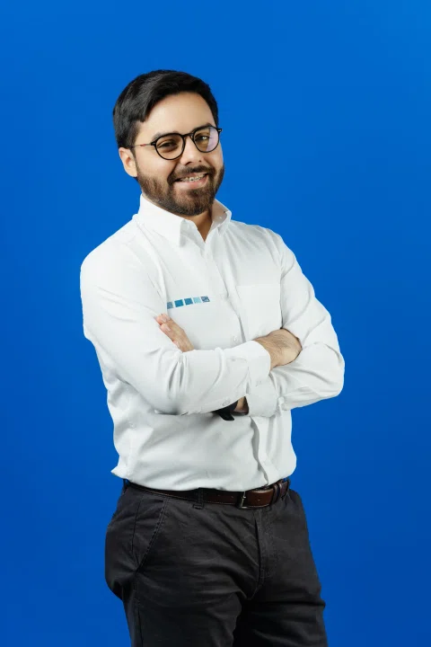Retrato profesional de un hombre con camisa blanca sobre fondo azul.
