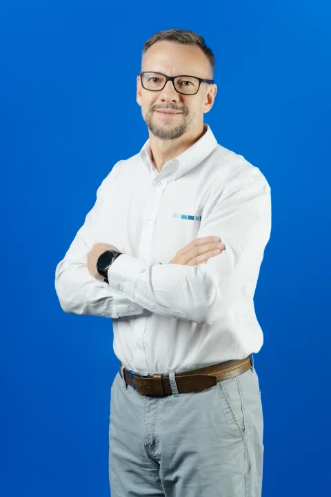 Retrato corporativo de hombre con lentes sobre fondo azul.