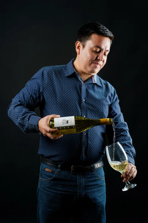 Retrato de un hombre sosteniendo una botella de vino y sirviendo una copa en estudio.