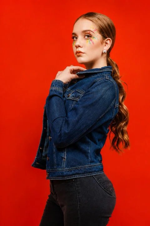 Retrato de una mujer con chaqueta de mezclilla sobre fondo rojo.