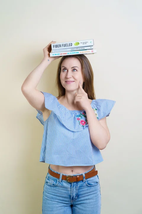 Retrato de marca personal de una mujer sonriente sosteniendo libros sobre su cabeza.