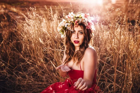 Retrato editorial de una mujer con vestido rojo y flores en un campo.