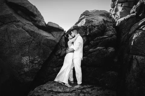 Retrato en blanco y negro de una pareja vestida de blanco entre grandes formaciones rocosas.