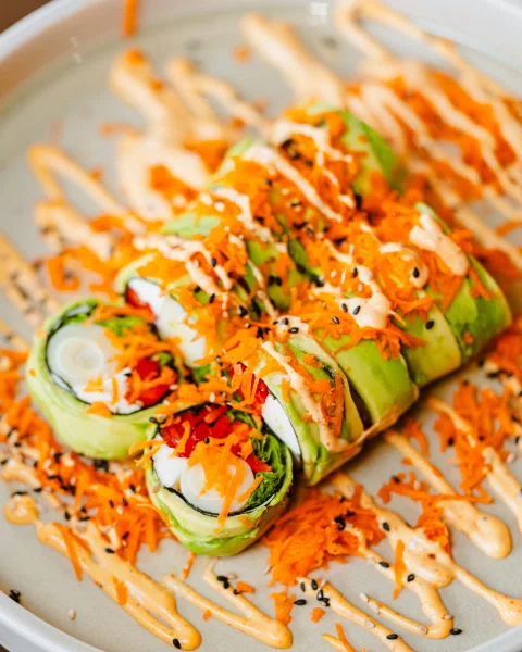 Roll de sushi cubierto de palta con salsa y semillas.