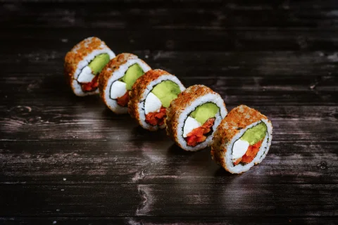 Roll de sushi con palta salmón y vegetales sobre mesa oscura.