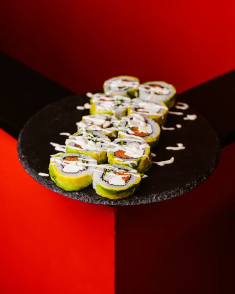 Roll de sushi sobre plato negro y fondo rojo.