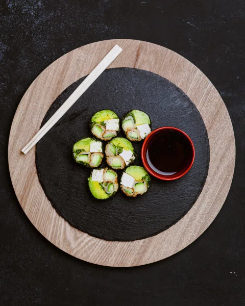 Rolls pequeños de sushi con salsa de soya sobre tabla circular.