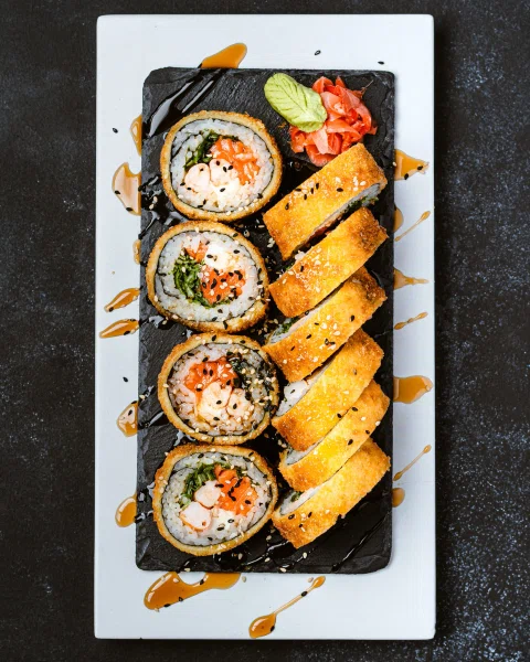 Rolls de sushi con cobertura dorada sobre plato rectangular.