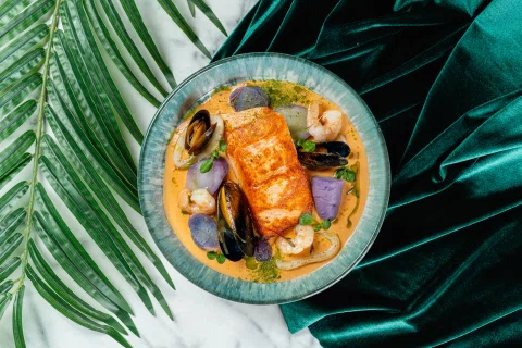 Salmón con mariscos y vegetales servido en un plato azul.