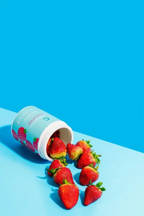 Suplemento de frutilla presentado con fruta fresca sobre fondo azul.