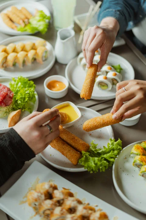 Personas comparten distintos platos de sushi alrededor de una mesa.