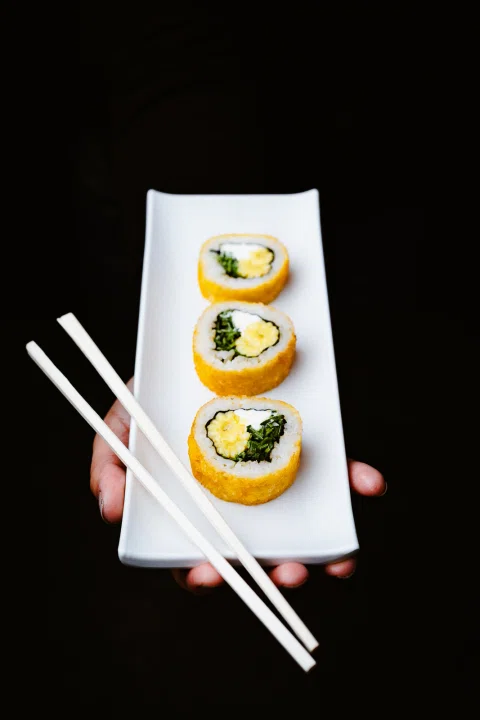 Tres piezas de sushi presentadas en un plato blanco sobre fondo negro.