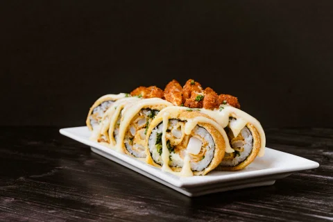 Rolls de sushi con salsa blanca servidos en un plato rectangular.