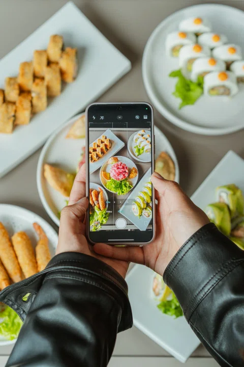 Persona fotografía una mesa con sushi usando un teléfono móvil.