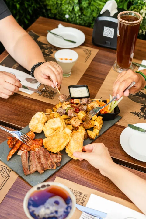 Tabla abundante de carnes papas y acompañamientos compartida.