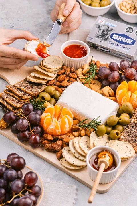 Tabla de aperitivo con quesos frutas y mano sirviendo.