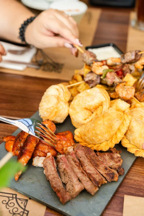 Tabla de carnes y papas mientras una persona se sirve.