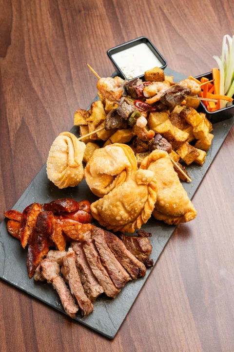 Tabla de carnes papas y vegetales en vista cercana.
