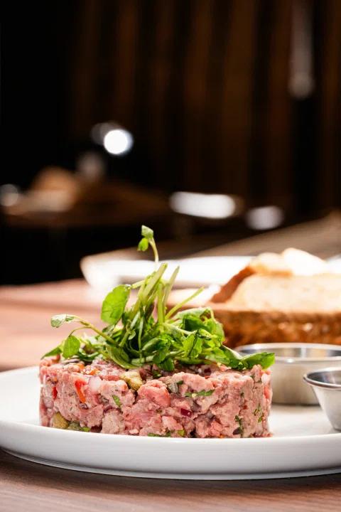 Tartar de carne con hojas verdes en ambiente interior.