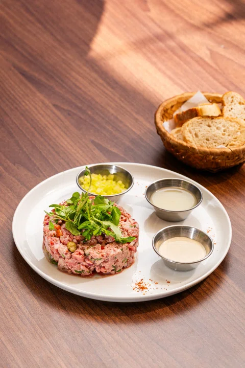 Tartar de carne con salsas y pan.