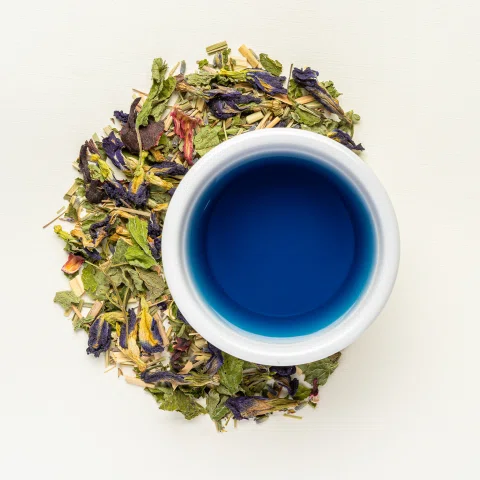 Taza azul rodeada por mezcla de hierbas secas.