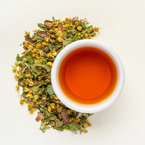 Taza de té ámbar rodeada por hierbas y flores secas.