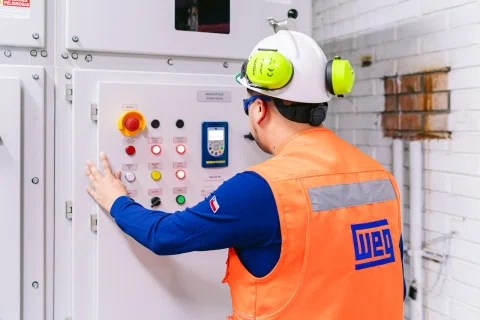 Técnico WEG operando panel de control industrial.
