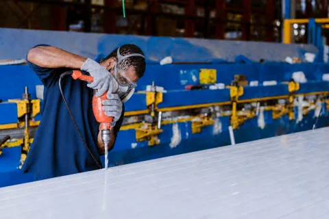 Trabajador perfora una estructura metálica dentro de una fábrica.