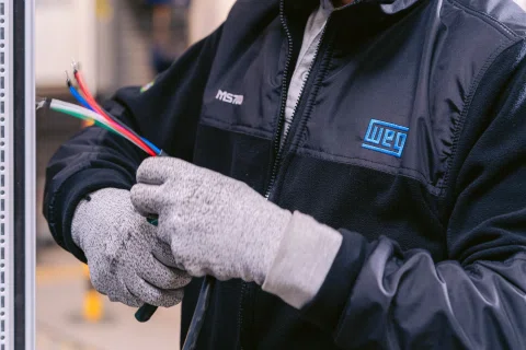Trabajador WEG manipulando cableado con guantes.