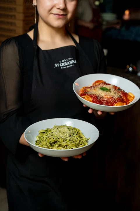 Trabajadora mostrando pasta verde y plato con salsa roja.