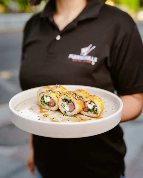 Trabajadora de Puerto Rolls sosteniendo plato de sushi.