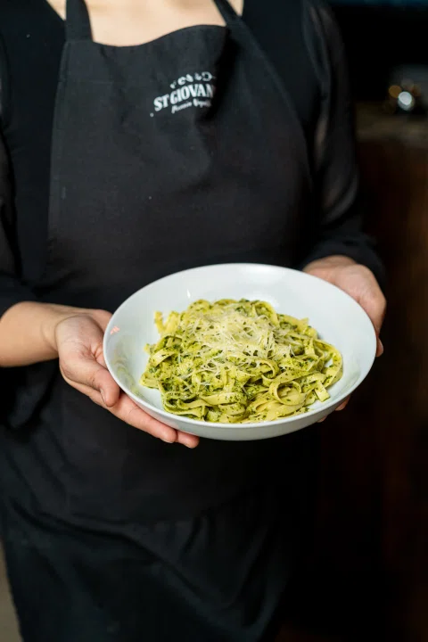 Trabajadora sosteniendo plato de pasta verde.