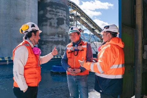 Tres trabajadores conversando dentro de faena industrial.