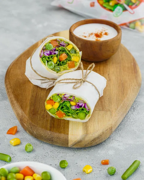 Wrap de vegetales servido sobre tabla de madera junto a un bowl de salsa.